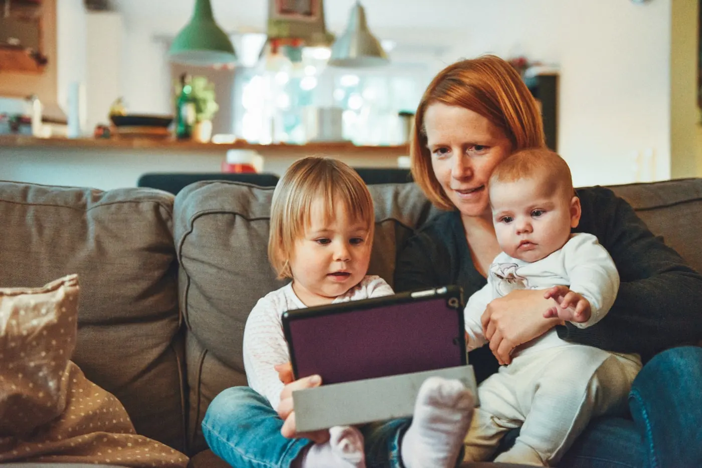 Madre con sus dos hijos pequeños usando una tablet en el sofá